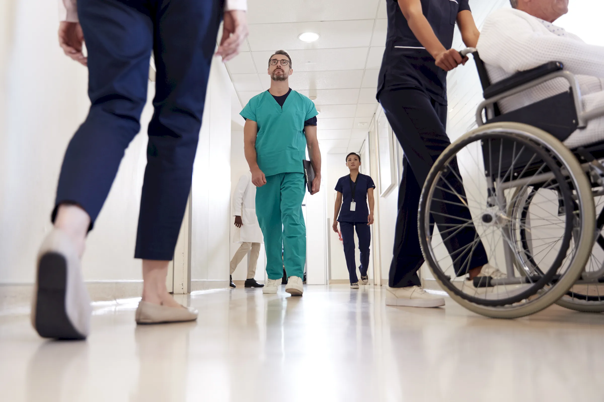 Staff and a patient in a wheelchair moving through a hospital corridor.