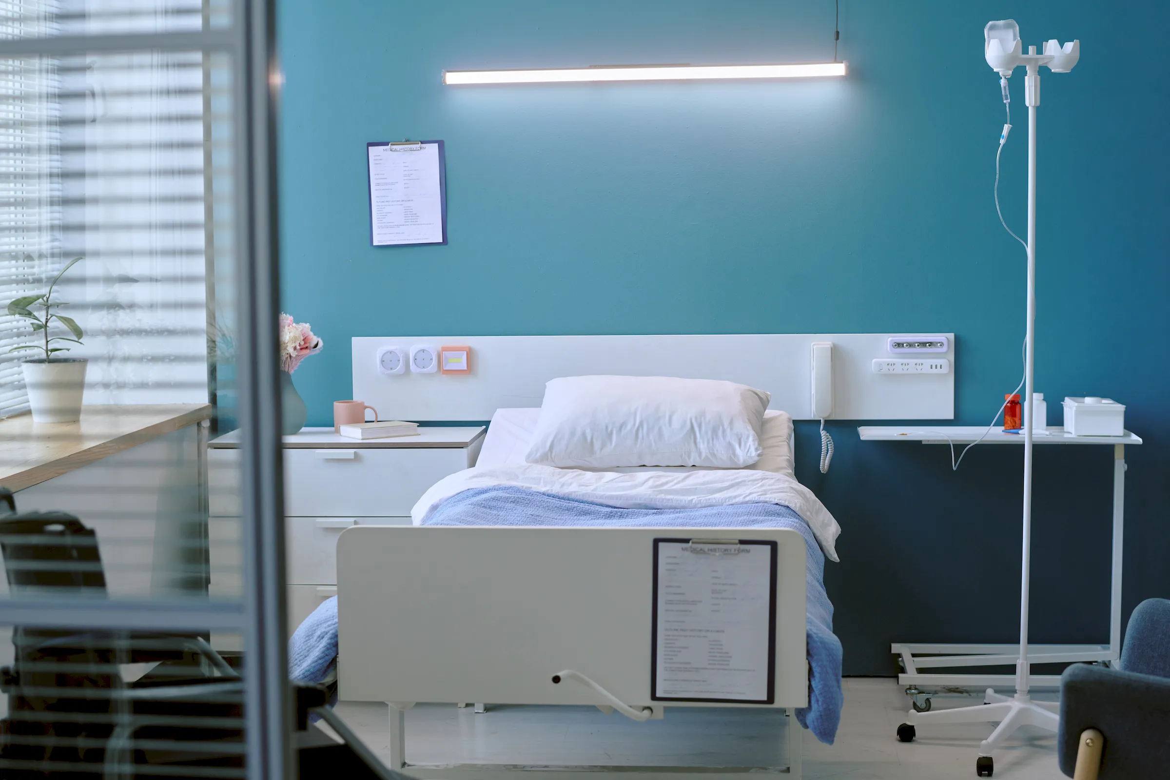 An empty hospital bay with a made bed and an IV stand.